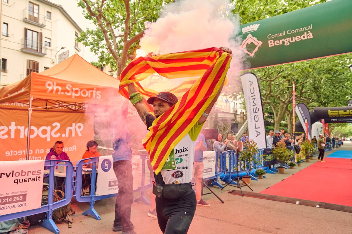 Un corredor creua la línia d’arribada amb una gran bandera catalana estesa al braç.