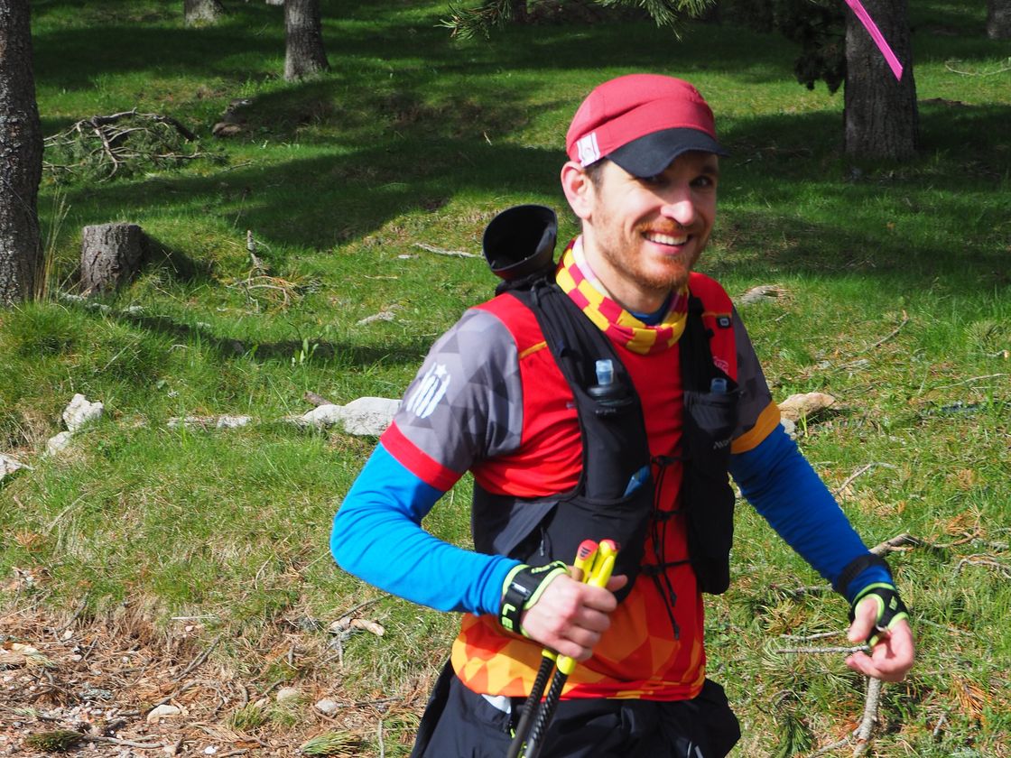 Corredor amb bastons i el dorsal 75 somrient en un corriol de bosc.